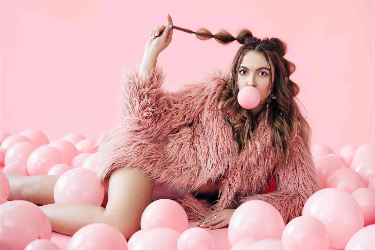 ragazza con pellicciotto rosa tra palloncini dello stesso colore e bolla bubble gum in bocca